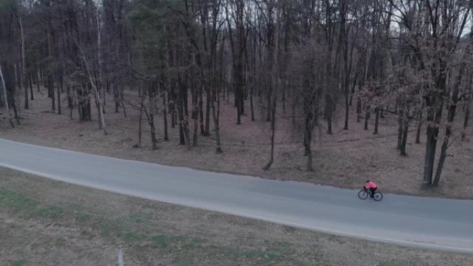 运动员在森林空车路上快速密集地踩着公路自行车。孤立的自行车骑行。戴着头盔和明亮夹克的骑自行车的人独自