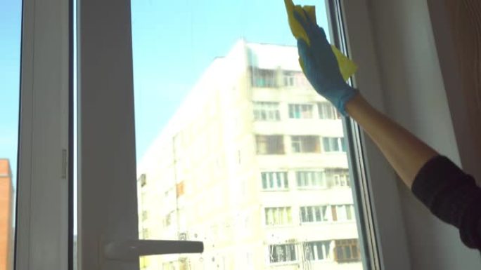 女人用蓝色手套洗窗户，用抹布擦玻璃。