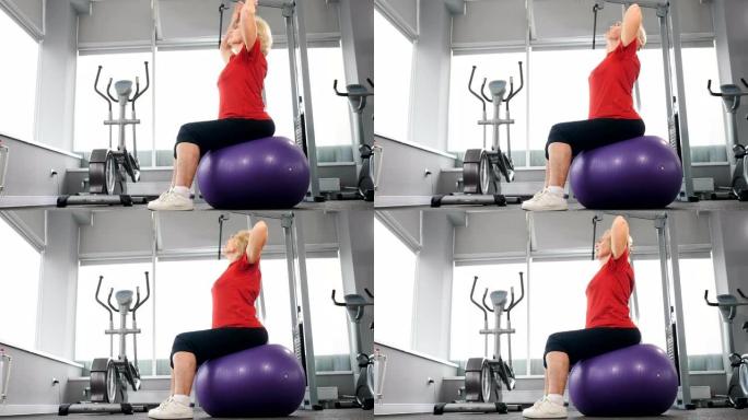 健身房里开朗的高级运动员在健身球上锻炼。运动养老金领取者的概念。老年妇女坐在健身球上。4k拍摄