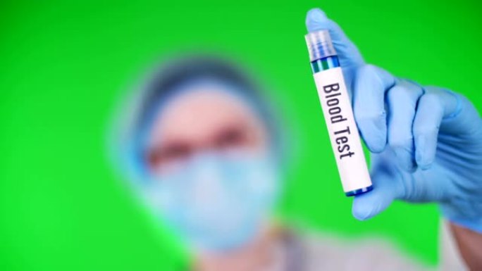 绿色背景。特写镜头，医生的手在蓝色的医疗手套上握着试管，上面刻有血液测试铭文。医生戴着医疗帽，口罩。