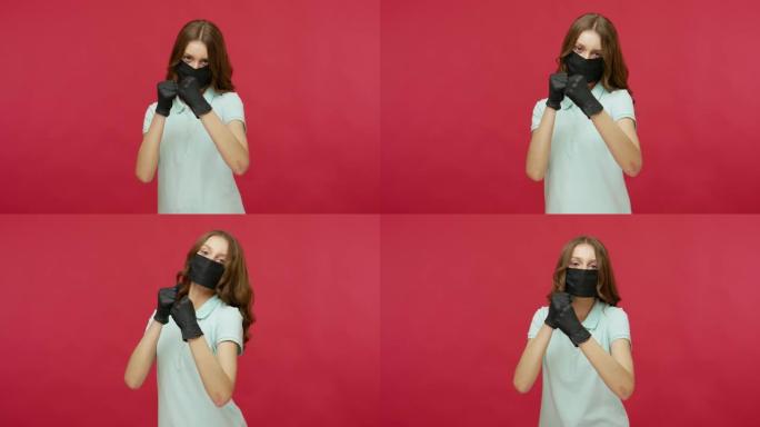 穿着黑色卫生面具和手套的女人用拳头拳打，拳击到相机，与传染病作斗争