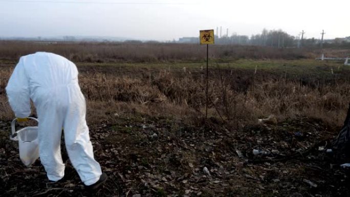 一个戴着防毒面具和防护服的人收集垃圾，污染指示器，背景中的植物