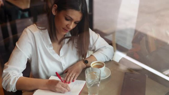 年轻女性作家坐在咖啡馆里，在笔记本上写笔记