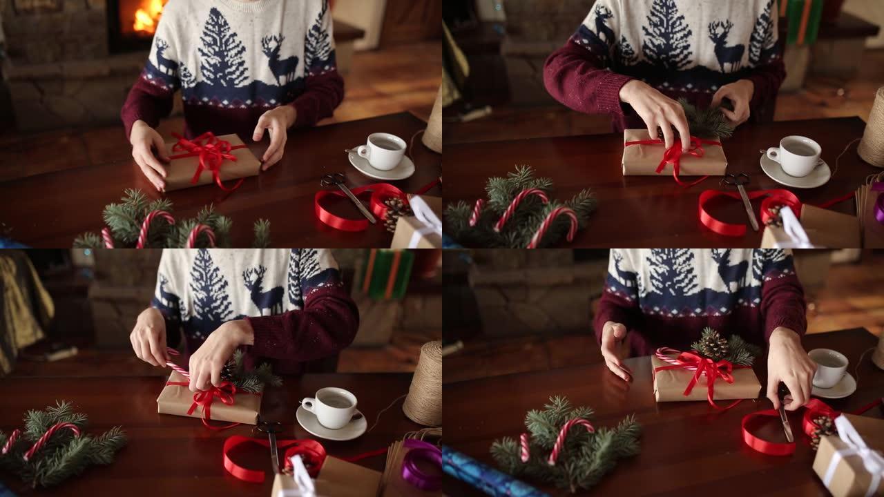 近距离观察人的双手在壁炉附近的圣诞节假期礼物上系弓。男性用纸包装礼物盒，用杉木树枝，圆锥体，木桌上的