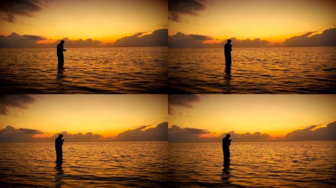 日出时站在海洋中祈祷/冥想的人的剪影