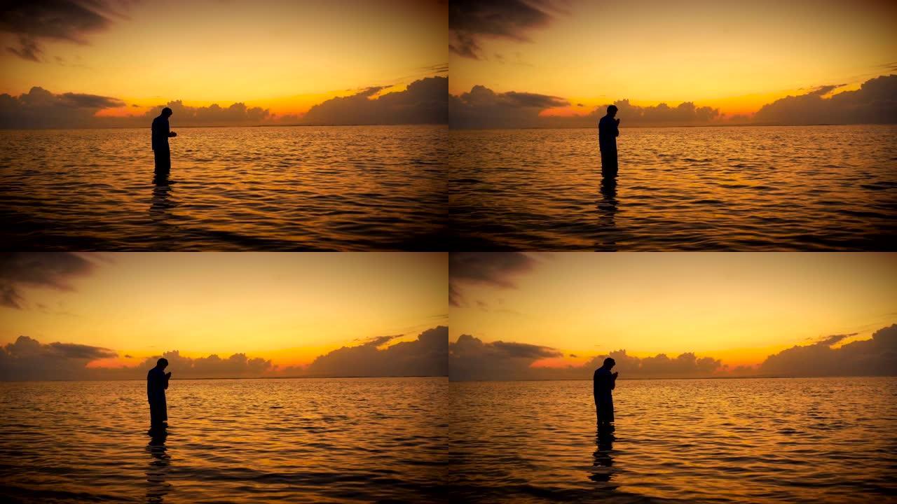 日出时站在海洋中祈祷/冥想的人的剪影