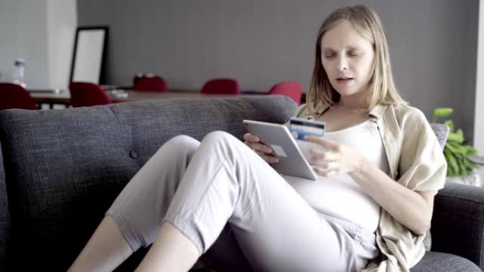专注的孕妇使用平板电脑在线购物