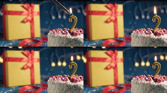 白色生日蛋糕2号点火器燃烧的金色蜡烛，蓝色背景带灯和用红丝带绑起来的礼物黄色盒子。特写