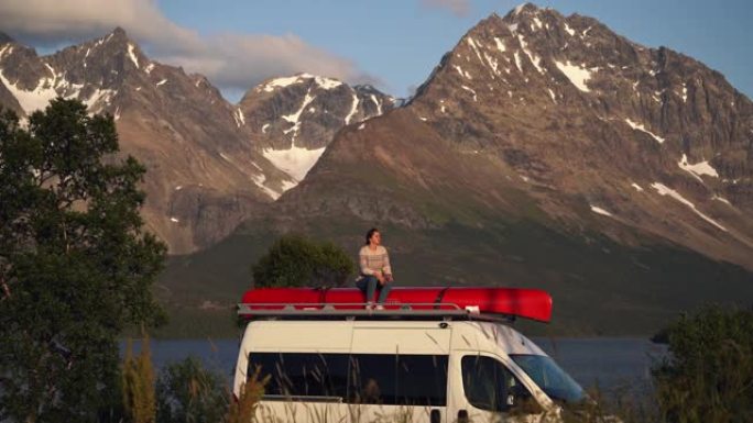 女人坐在湖边的露营车顶上