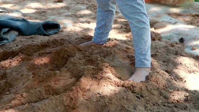 孩子站在沙堆上，用铁锹铲沙