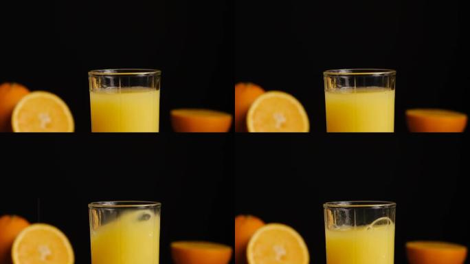 冰块落在黑色背景上的橘子果汁或柠檬水玻璃中。用天然成分准备健康早餐。慢动作。