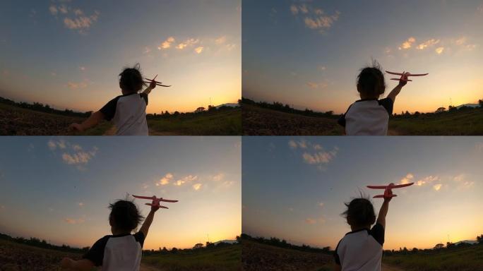 一个快乐的小女孩的慢动作在日落背景下与玩具飞机一起奔跑。幸福家庭和童年梦想的概念。