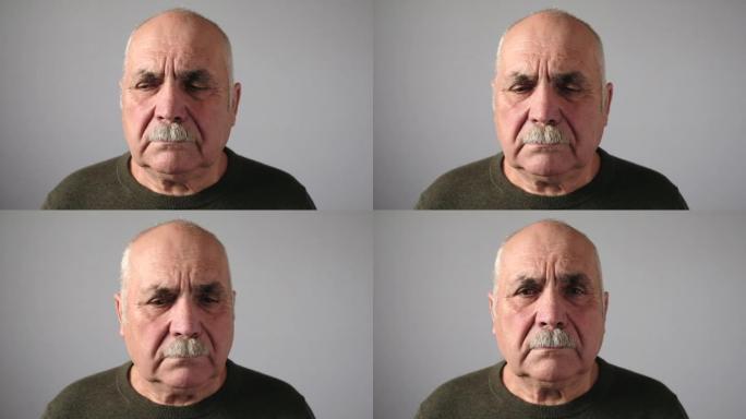 特写头和肩膀视频一个秃头的老人的肖像，留着小胡子，看着相机，左右，在灰色背景下带着悲伤和沮丧的面部表