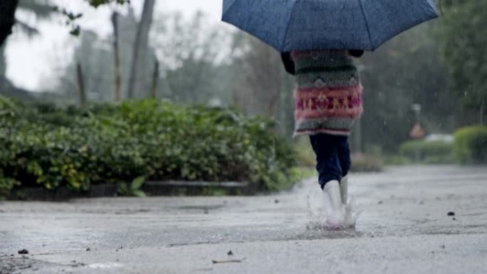 一个小女孩在水坑里跳伞的慢动作在雨中撑着伞