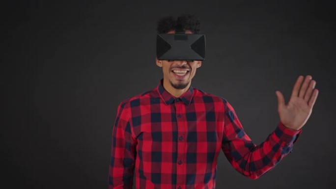 穿着衬衫微笑的非洲男子在黑暗背景下孤立的虚拟现实眼镜中问候某人