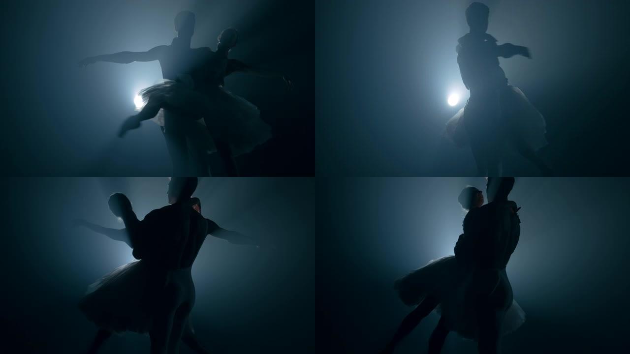 优雅的芭蕾舞演员和她的男性伙伴在黑暗中与泛光灯背光跳舞的古典或现代芭蕾舞元素。一对夫妇在黑色背景的烟