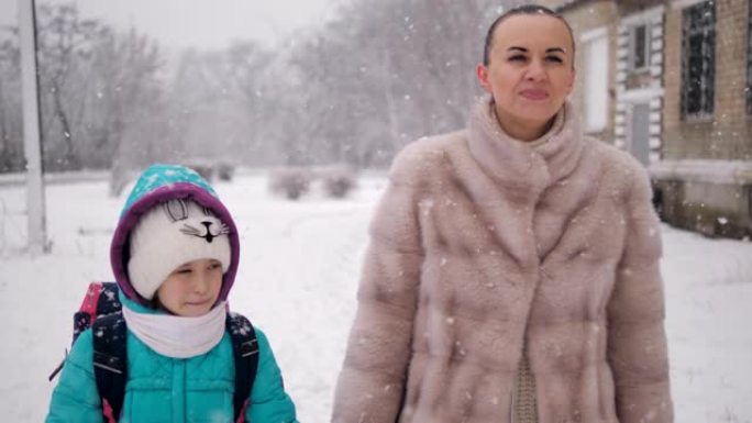 母亲和女儿牵着手在雪地里放学回家。