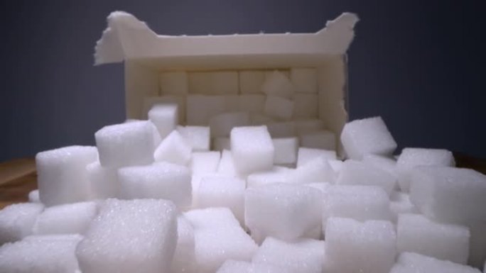 Macro dolly拍摄了滑过方糖的镜头，然后滑入木桌上的纸箱中。不健康食品甜味剂，甜水晶方块