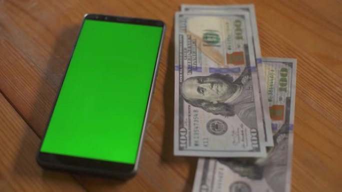 男人在桌子上的手机屏幕触摸板旁边折叠百美元钞票。绿屏手机模型。货币现金色度关键概念。技术和经济。个人
