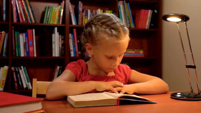 六岁的女孩坐在台灯的灯光下看书