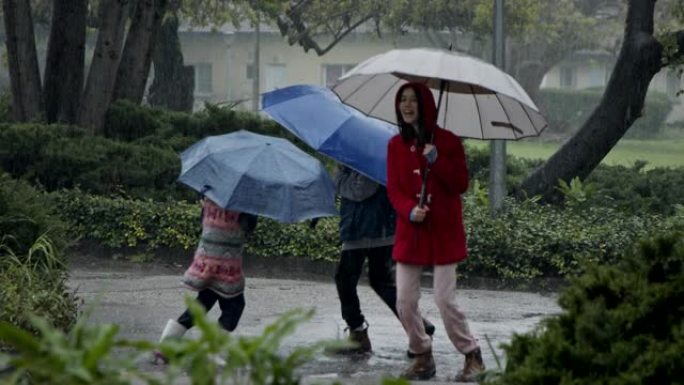 三个孩子的慢动作在雨中快乐奔跑，用雨伞的水坑