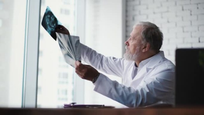 成年男性医生在大窗户的桌子上检查x射线和MRI扫描