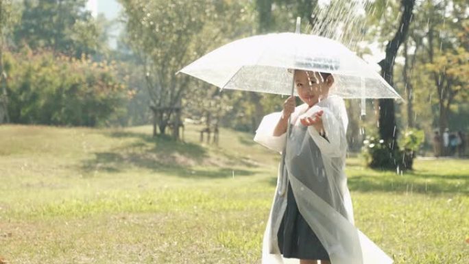 小女孩穿雨衣透明伞的慢动作镜头在晨光下的花园里玩雨