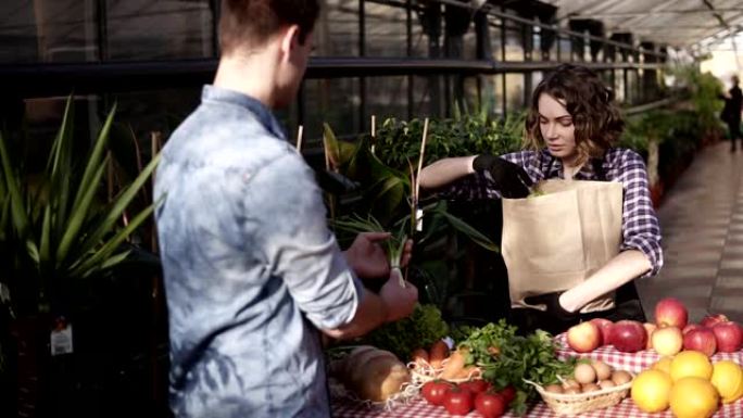 布鲁内特 (Brunette)，穿着围裙的欧洲女售货员帮助顾客选择，将一堆绿色沙拉放在棕色纸袋中，供