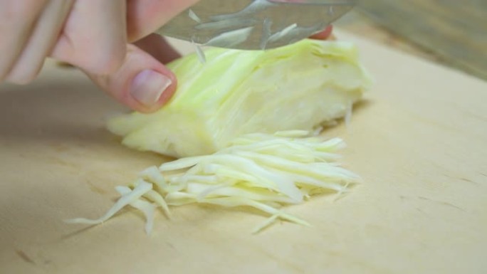 厨师在木砧板上切碎纳帕卷心菜的亚洲凉拌卷心菜的特写镜头，选择性聚焦。健康食品准备。