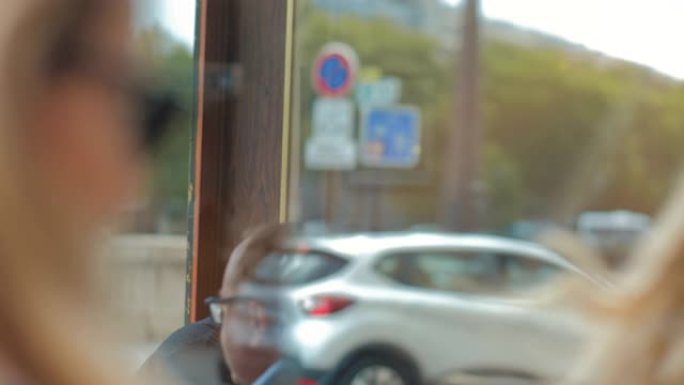 一个戴着墨镜的金发美女，看着她在商店橱窗里的倒影。汽车在后台经过。法国巴黎