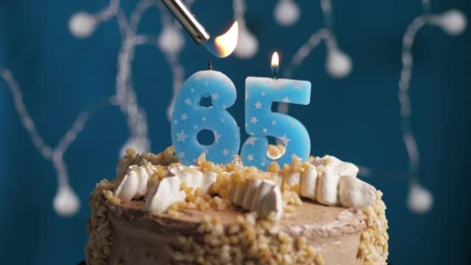 蓝色背景上有65号蜡烛的生日蛋糕。蜡烛着火了。慢动作和特写视图