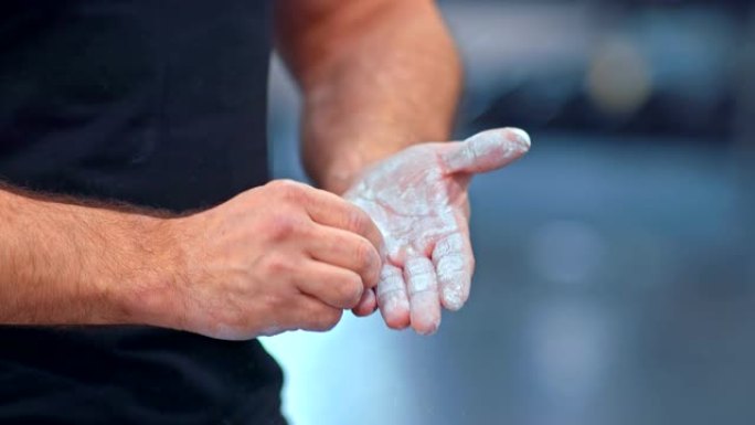 男运动员用粉笔擦手，训练的开始。运动员拍手，粉笔从他的手中飞走。健身房。特写。