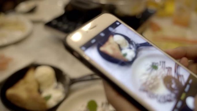 年轻的亚洲女人在桌子上用手机拍照冰淇淋布朗尼。
