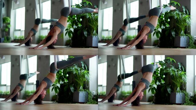 中等身材的年轻女子在反重力瑜伽工作室做空中瑜伽腹肌运动摇摆双腿左右倒挂在吊床上