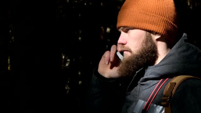 一个戴着帽子的大胡子男人在针叶林里用手机说话。难以到达的地方的蜂窝通信概念