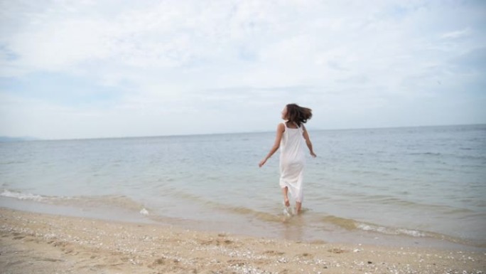 快乐的亚洲女人赤脚走在热带夏季海滩上。女人在沙滩上沿着海水和沙子的波浪行走。享受赤脚自由行走户外。放