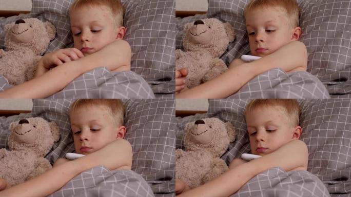 一个生病的小男孩躺在床上，体温计和泰迪熊的特写镜头。