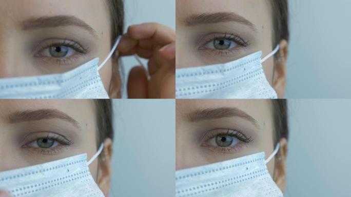 女性脸部极度特写戴上保护性医用口罩，用于病毒感染的预防和保护。戴着医用面具的年轻女性。流行病病毒的恐