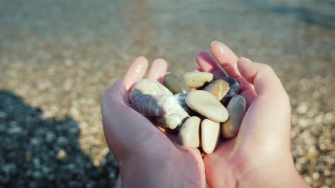 一个人坐在海边的海滩上时拿着一把鹅卵石