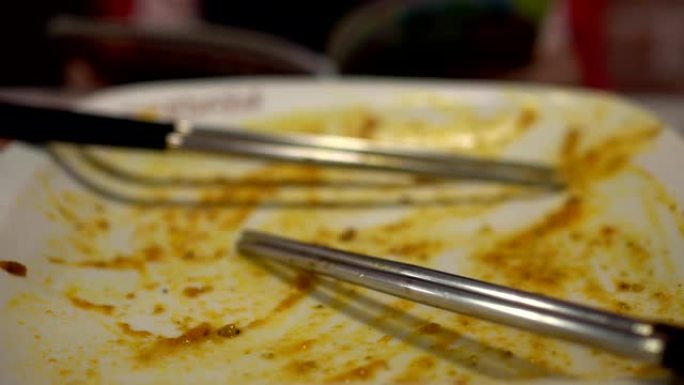 在餐厅吃完食物后空盘子。用两双筷子。背景模糊是一个小女孩在饭后看书。