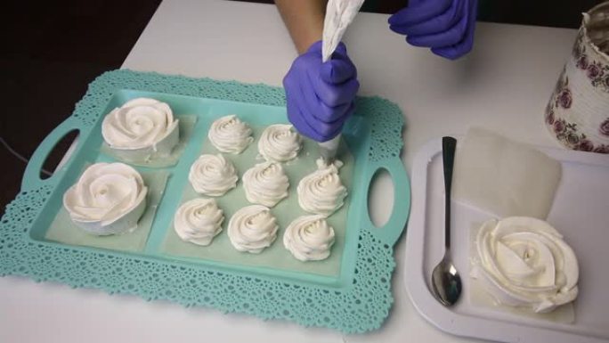 托盘上放着玫瑰形式的棉花糖。一个使用糕点袋的女人在旁边形成各种形状的棉花糖。位于行中。