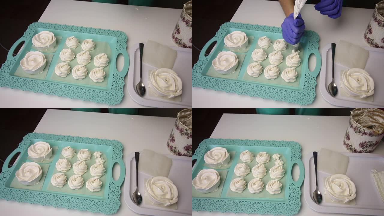 托盘上放着玫瑰形式的棉花糖。一个使用糕点袋的女人在旁边形成各种形状的棉花糖。位于行中。