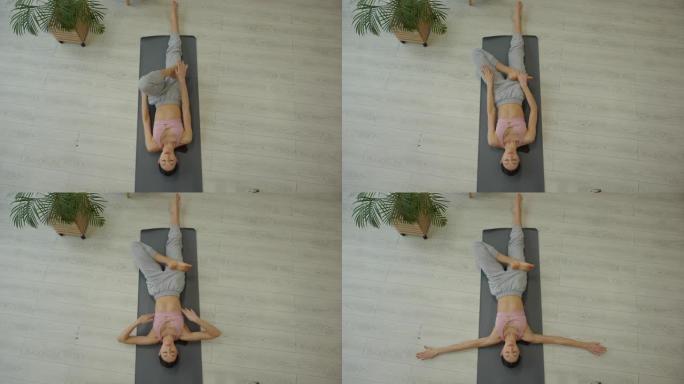 运动年轻女子躺在家里的垫子上练习瑜伽，从上面看