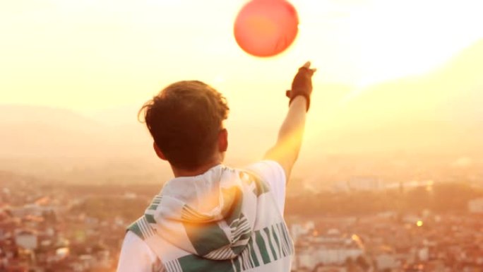 男孩的背后将红色气球抛向空中，上面写着文字，我在城市和美丽的日落前想念你