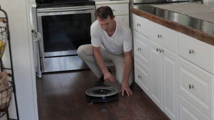 成年男子将圆形机器人吸尘器放在厨房地板上，切换