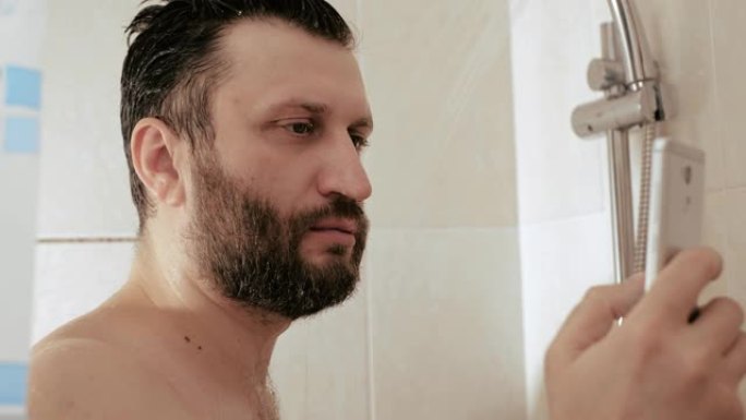 一个拿着电话洗澡的男人。一个大胡子的家伙在电话上阅读新闻时在水下洗头。互联网社交网络智能手机细胞成瘾