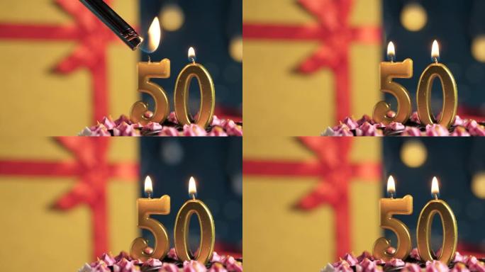 生日蛋糕50号点火器燃烧的金色蜡烛，蓝色背景礼物黄色盒子用红丝带绑起来。特写和慢动作