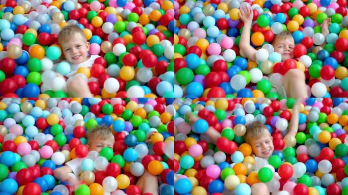 金发小男孩躺在游戏中心大干戏水池里的多色塑料球上。对着镜头微笑。肖像特写。在游戏室玩得开心。休闲活动