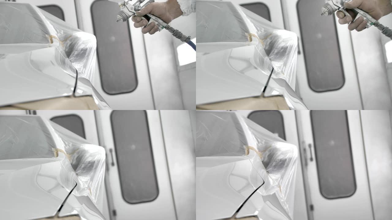在喷漆室中对白色汽车进行喷漆的过程。使用喷枪的人