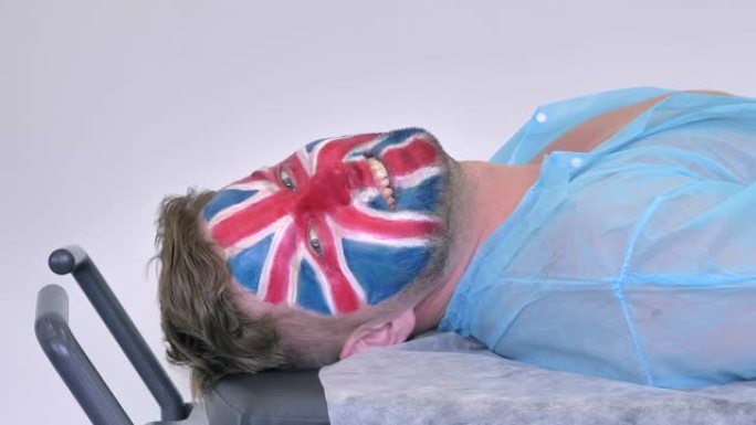特写，侧视图，英国人的肖像 (足球迷，英格兰国旗/英国国旗画在他的脸上) 在医院的病床上看着相机。希